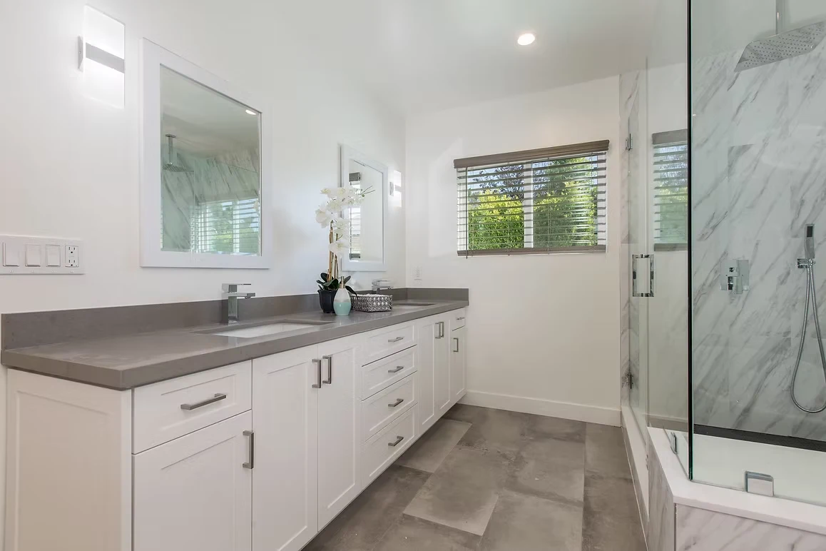 Modern bathroom with a white vanity, gray countertop, and glass shower.