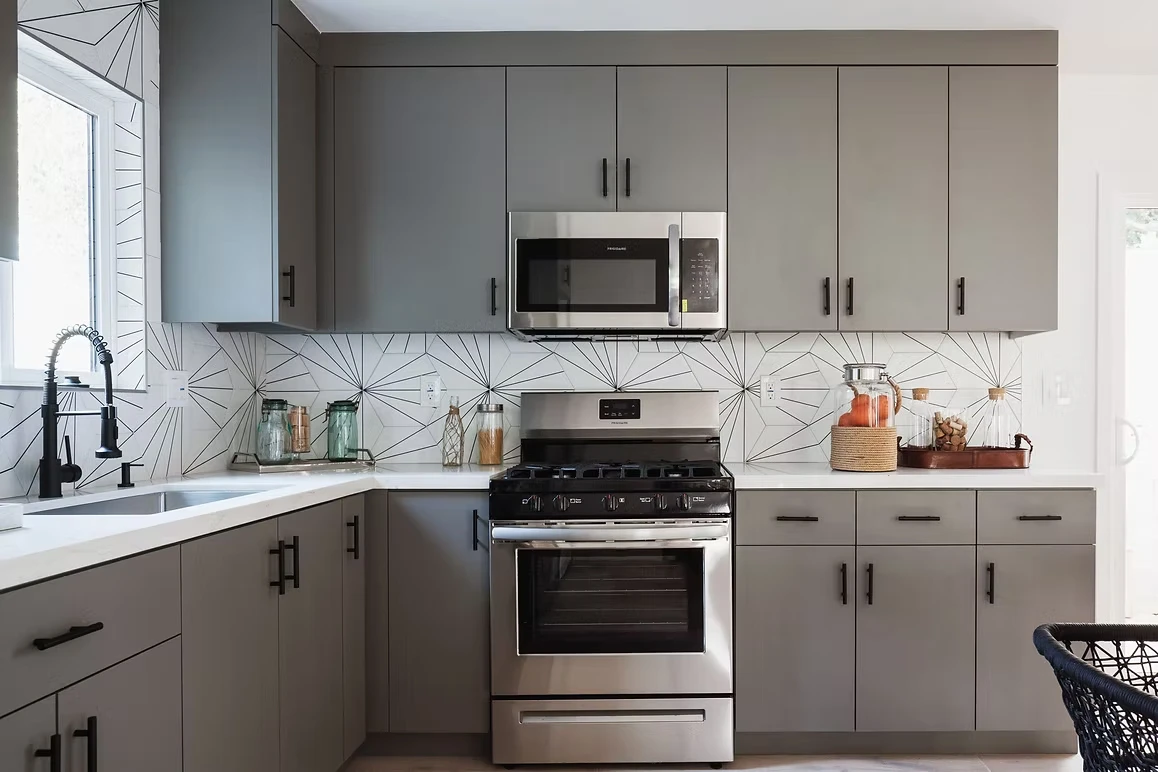 Modern kitchen remodel with gray cabinetry, stainless steel appliances, and geometric tile backsplash.