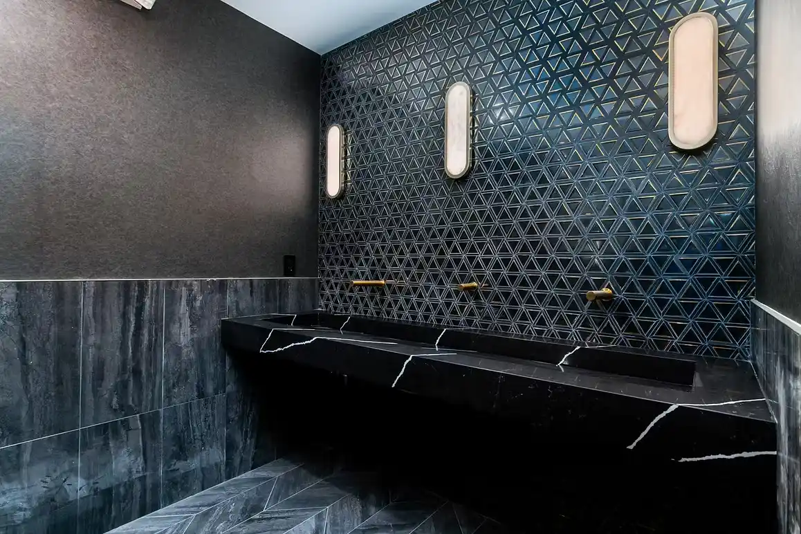 Chic bathroom with geometric tile wall, black stone sink, and modern lighting.