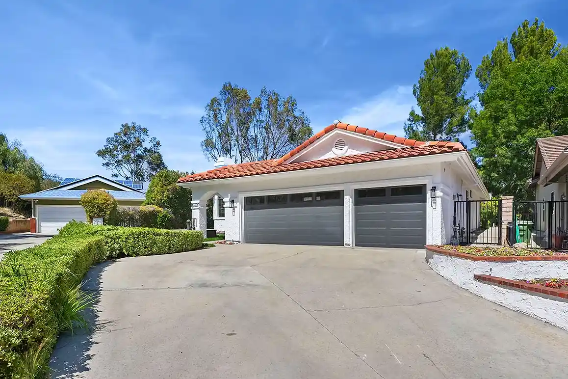 Exterior view of a home with a three-car garage, well-maintained landscaping, and a clear blue sky