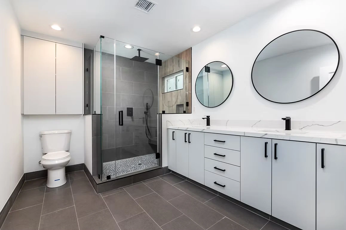 Modern bathroom with round mirrors, white vanity, and glass shower.