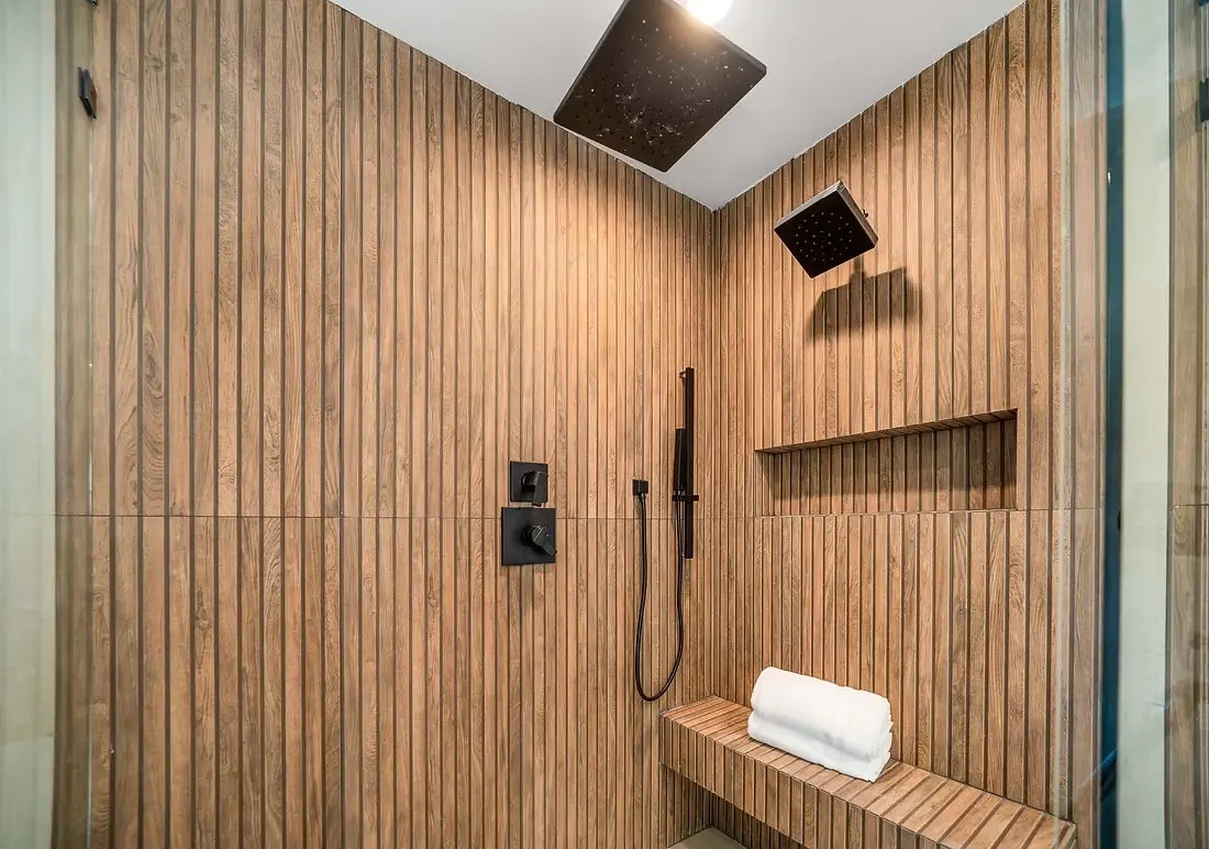 Stylish shower with wooden wall panels, bench, and black fixtures.