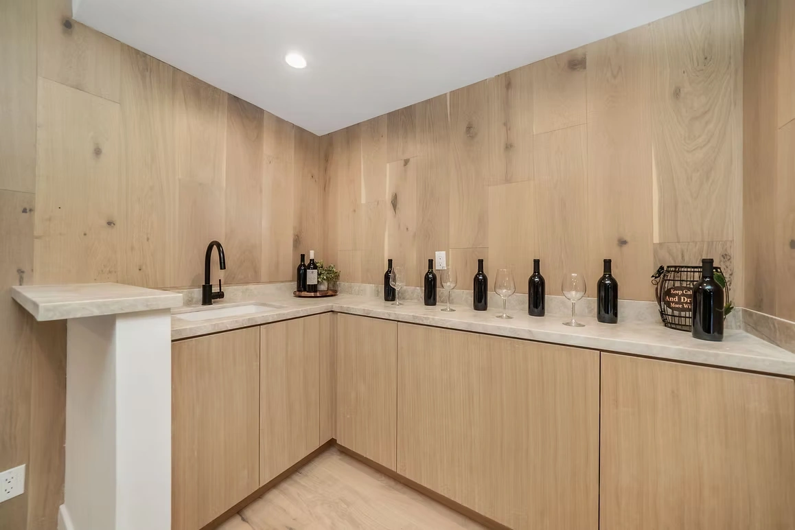 Custom wine bar area with wooden cabinets, marble countertop, and black faucet.