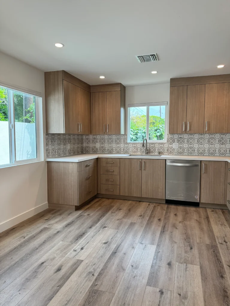 A view of the kitchen's corner showing the upper and lower wood cabinets, a white sink, and a large window.