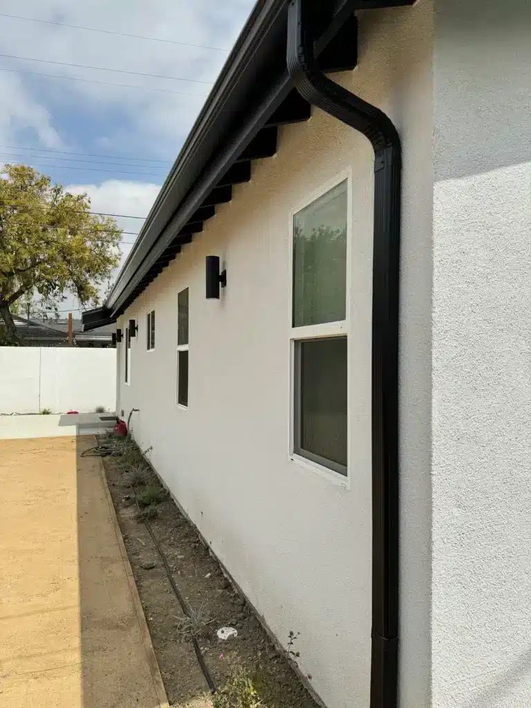 A close-up view of the side and rear corner of a modern light-beige stucco accessory dwelling unit (ADU).