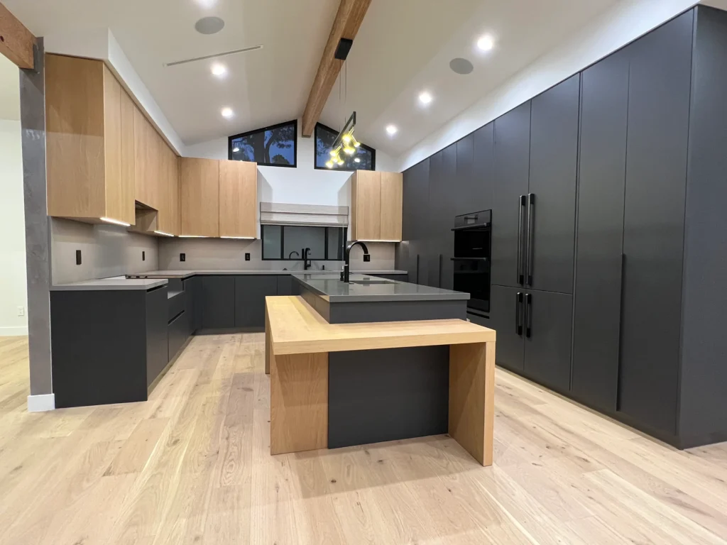 Kitchen view showing vaulted ceilings with wood beams and a mix of black and wood cabinetry.