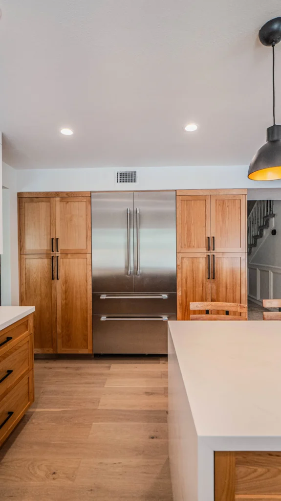A view of a large stainless steel refrigerator flanked by tall natural wood pantry cabinets.