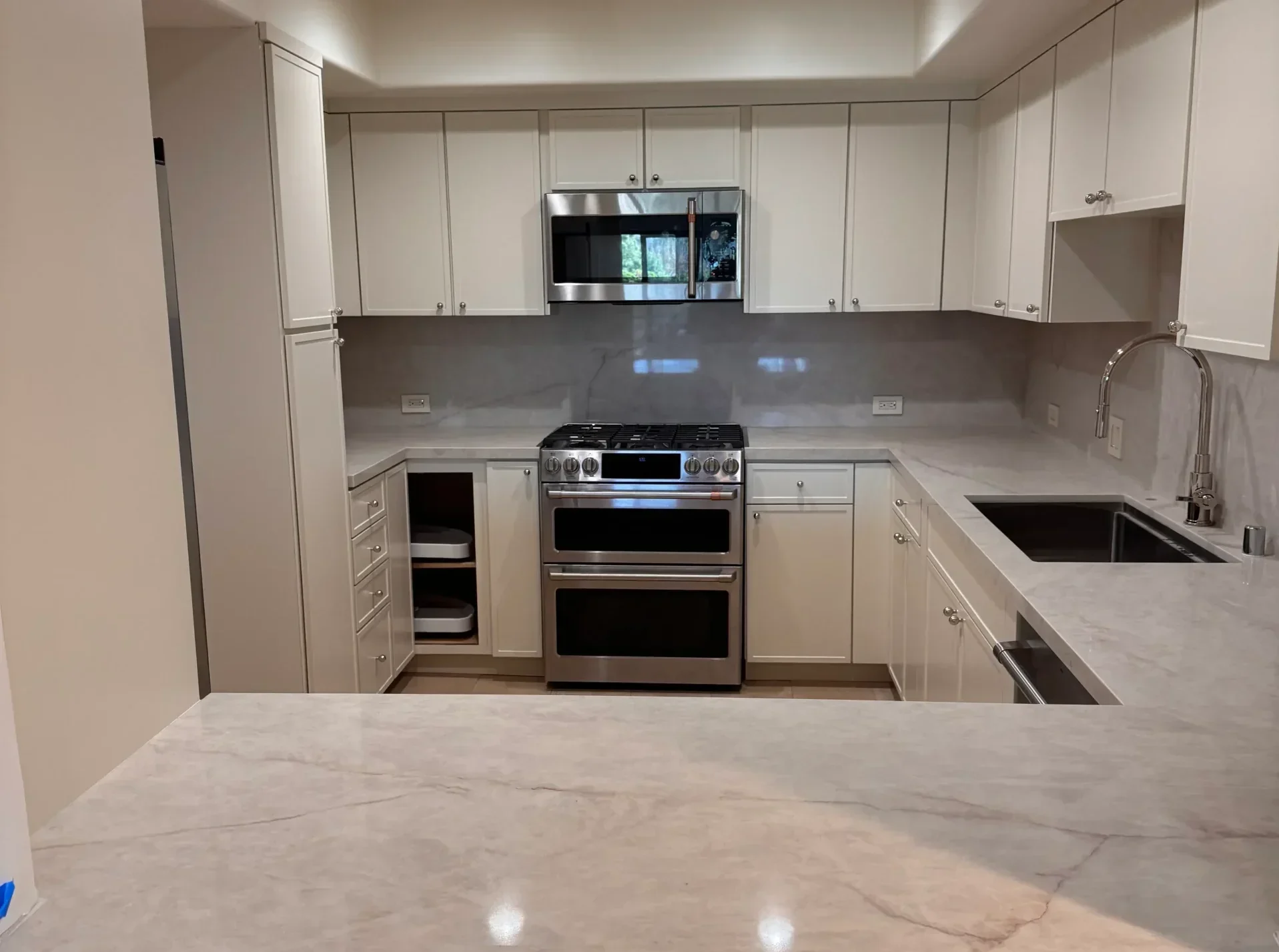A centered shot of a kitchen remodel featuring a stainless steel stove and white cabinetry.