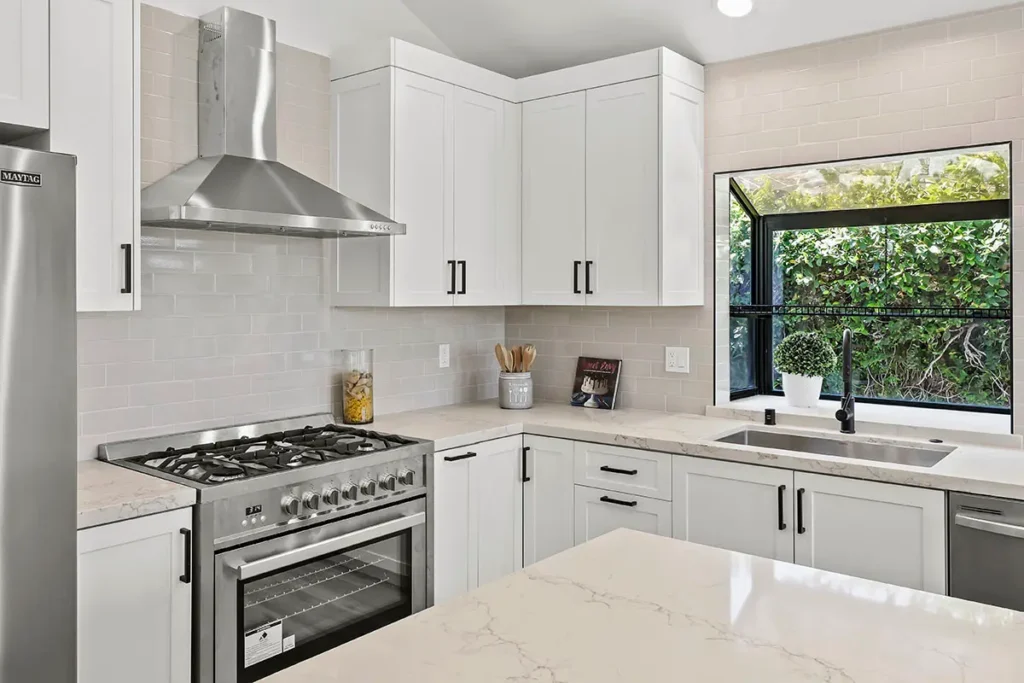 A kitchen corner with white shaker cabinets, a marble-style countertop, and a stainless steel gas range and hood.