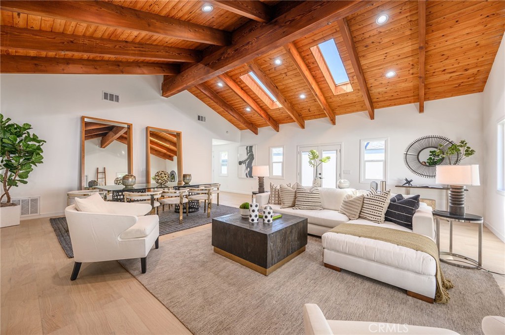 A large living room with high vaulted wood ceilings, skylights, white furniture, and a neutral rug - Nobel Builders