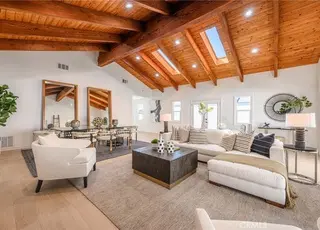A large living room with high vaulted wood ceilings, skylights, white furniture, and a neutral rug.