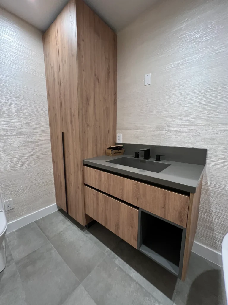 A bathroom vanity with a grey integrated stone sink and a tall wood storage cabinet.