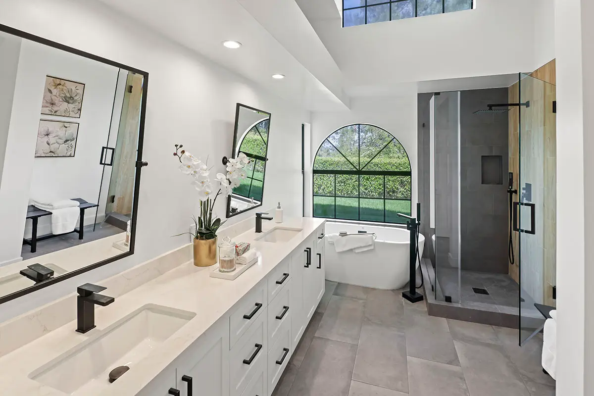 A wide view of a master bathroom showing the double vanity, glass shower, and soaking tub under a vaulted ceiling.