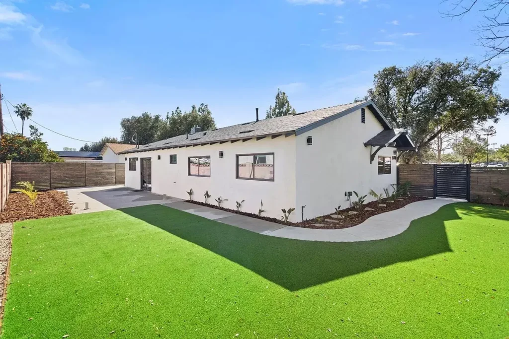 A white single-story home with a black roof and a vibrant green artificial grass lawn.