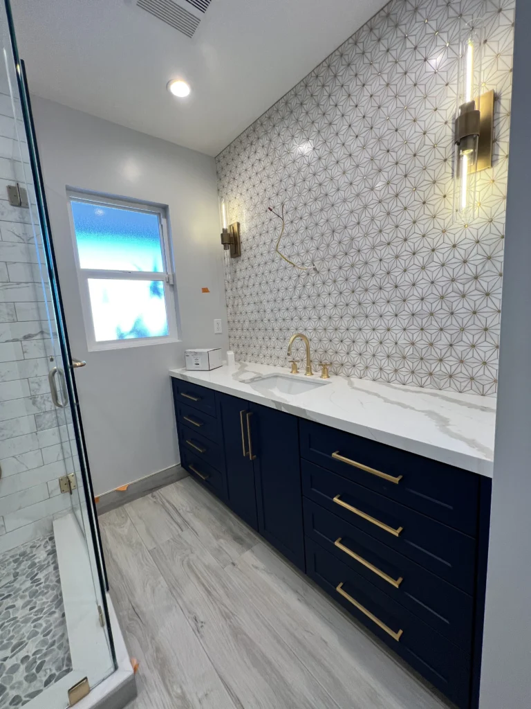 A bathroom vanity with navy blue cabinets, gold handles, and a geometric star-patterned tile backsplash.