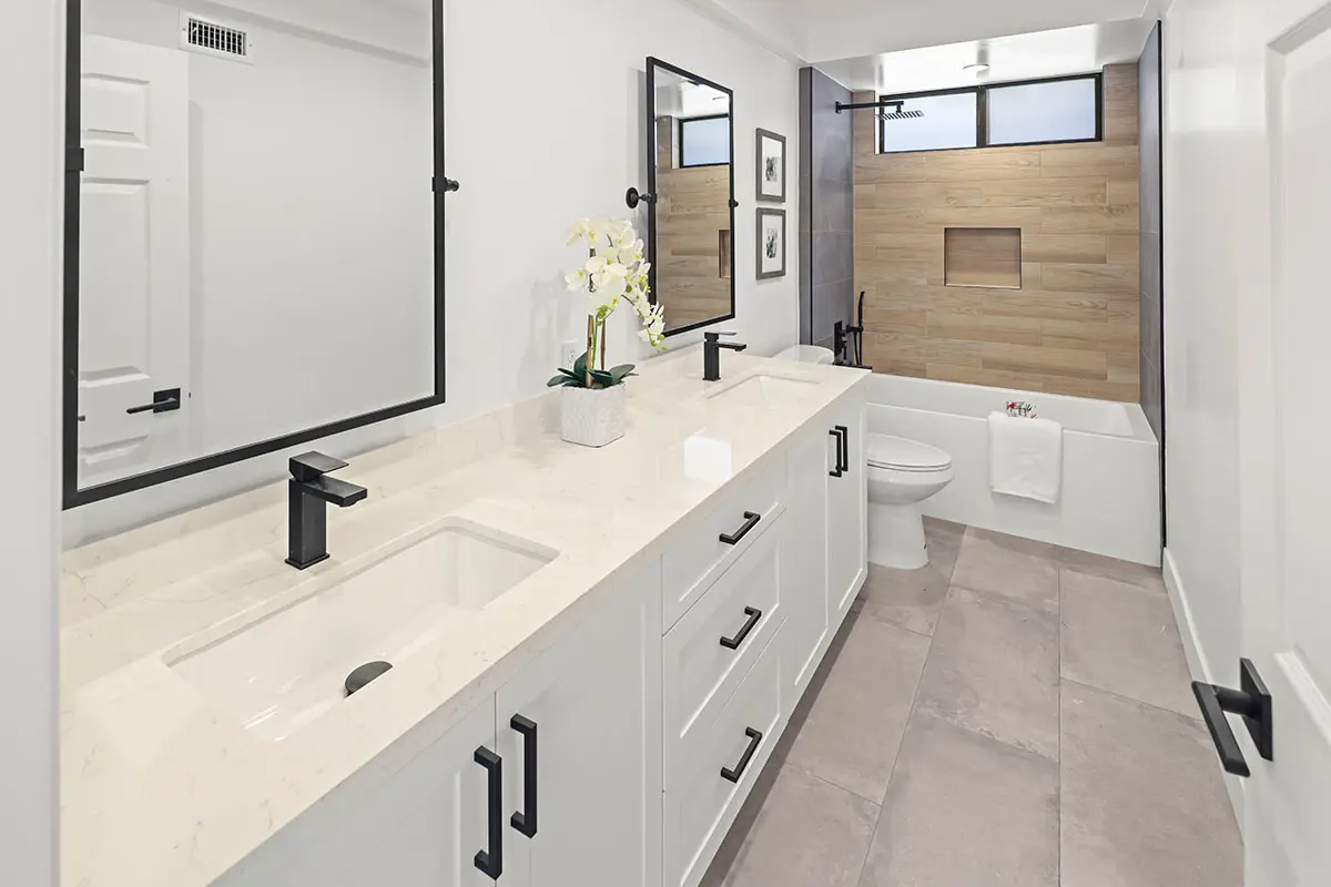 A long white bathroom vanity with black hardware, a rectangular sink, and a large black-framed mirror.