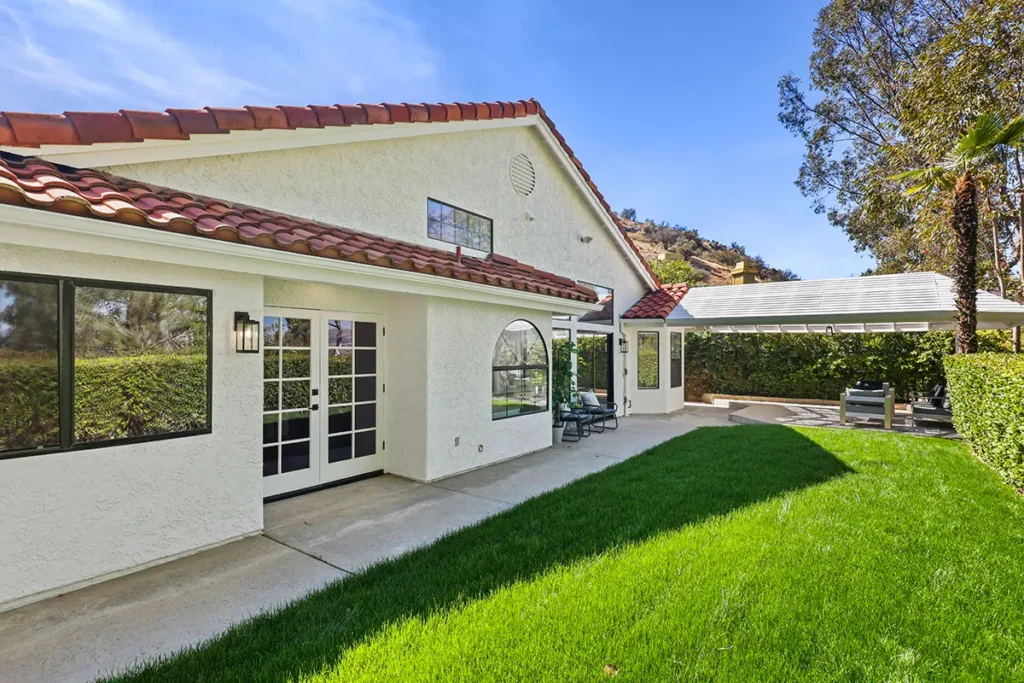 A view of a white stucco house with a red tile roof leading out to a vibrant green lawn under a clear blue sky.