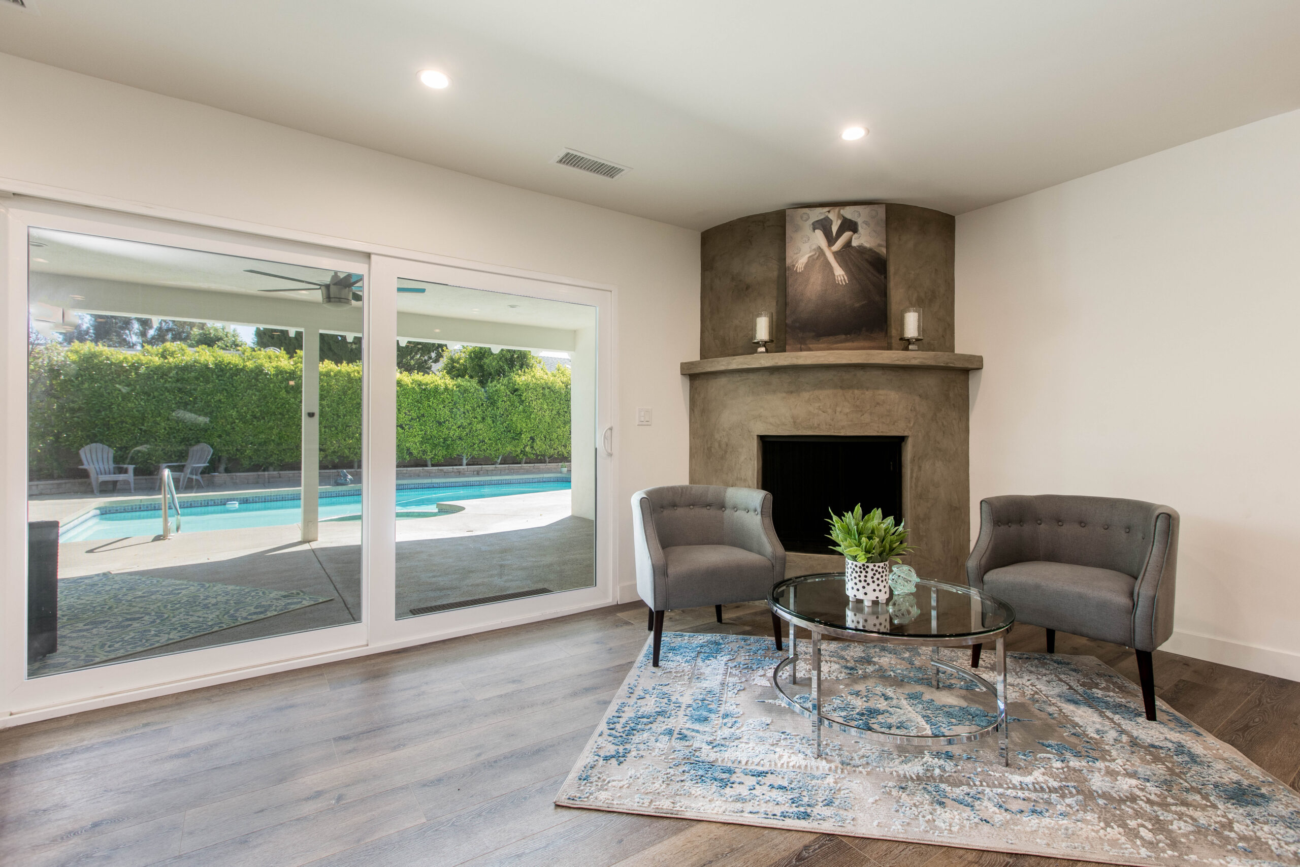 A cozy sitting area with a corner stone fireplace and large sliding glass doors opening to a backyard swimming pool.