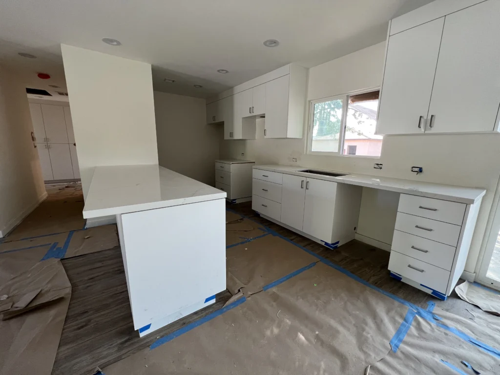 Brand new modern kitchen featuring white shaker cabinets, bright quartz countertops, and protective floor covering.